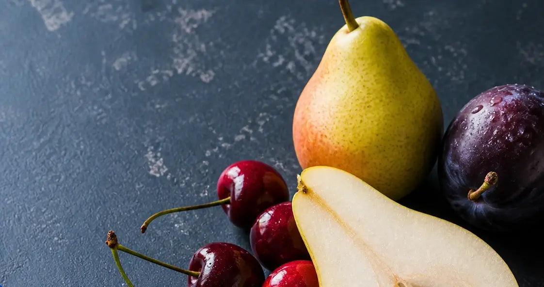 Fresh pears, cherries, plums, and pistachios arranged on a dark stone surface with cobalt blue linen