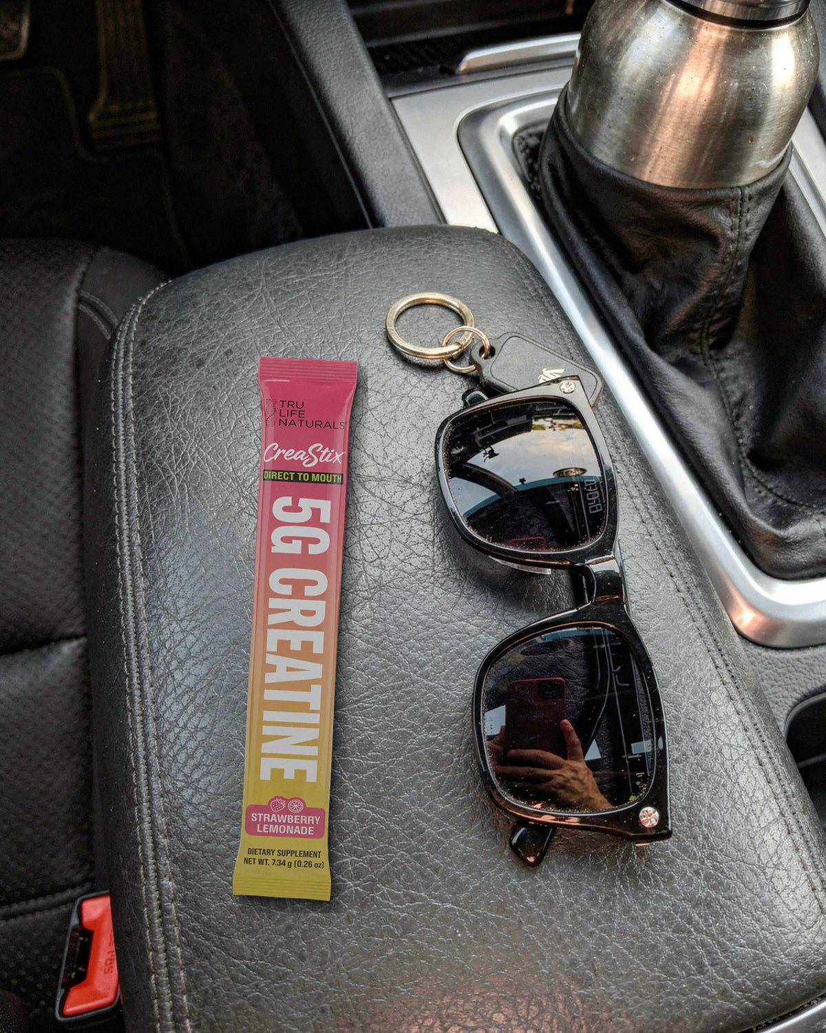 A Strawberry Lemonade CreaStix stick on a car armrest next to sunglasses and keys