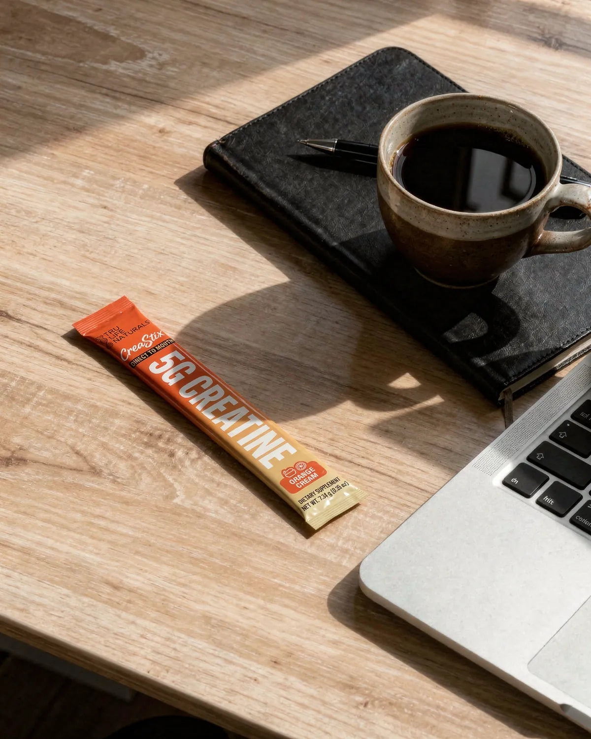 An Orange Cream CreaStix stick on a wooden desk beside a coffee cup and a laptop