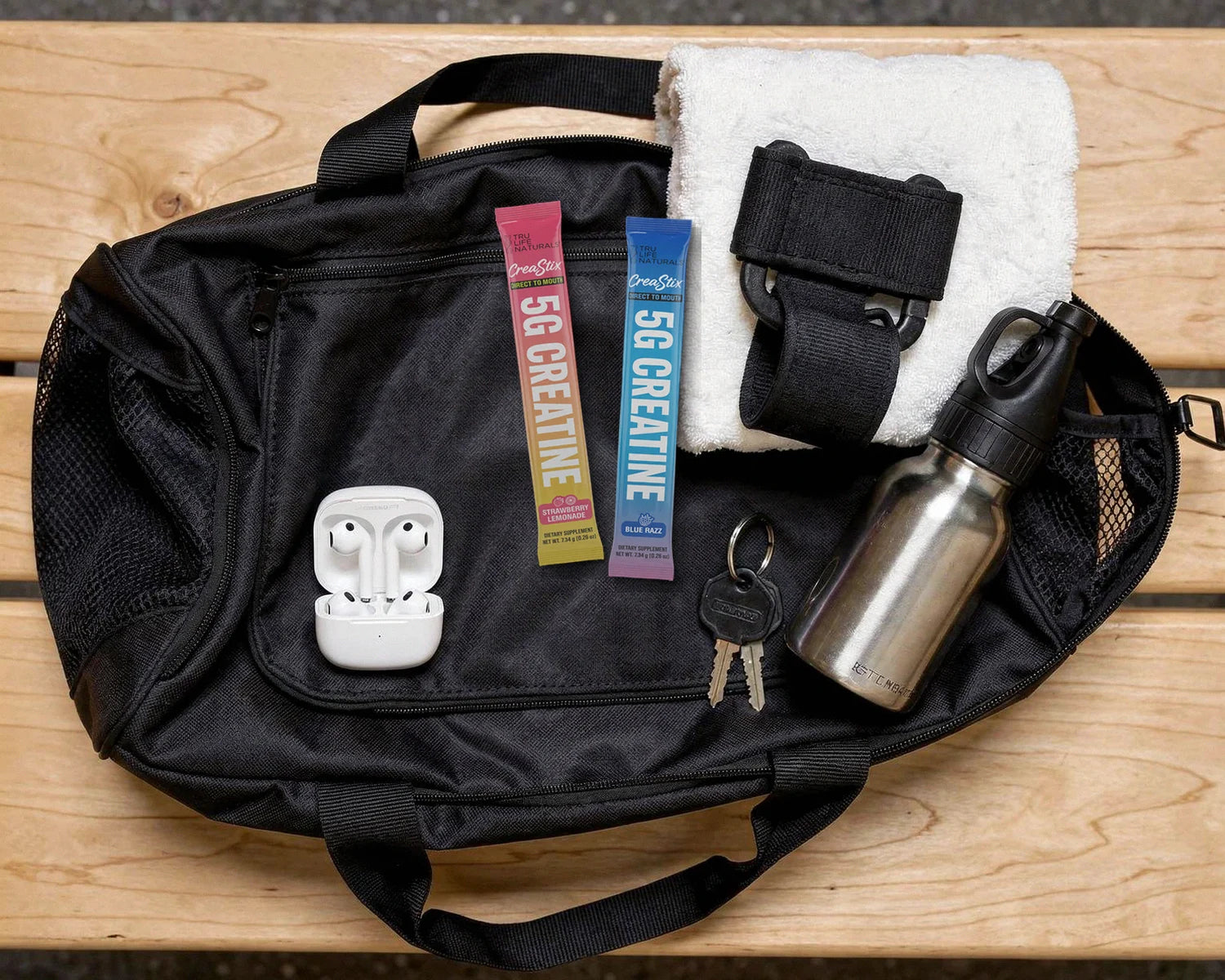 Strawberry Lemonade and Blue Razz CreaStix sticks on a gym bag next to earbuds, keys, a lifting strap and a water bottle