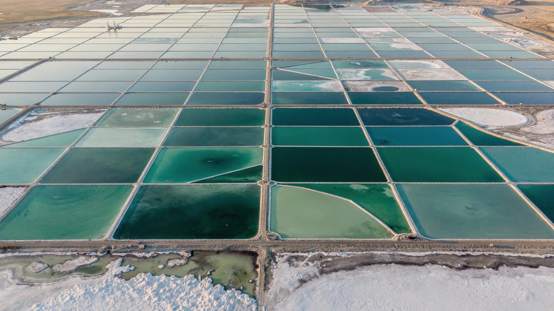 Aerial view of turquoise and teal solar evaporation ponds at the edge of the Great Salt Lake