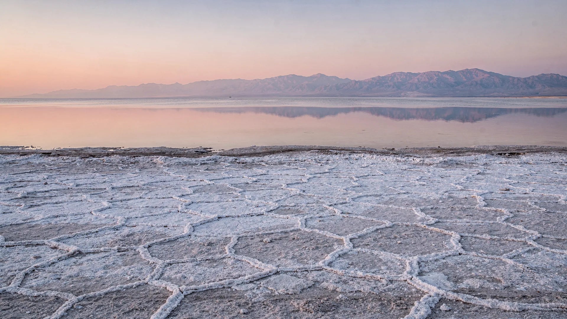 The Great Salt Lake at sunrise, a crust of white salt crystals in front of still water and distant mountains